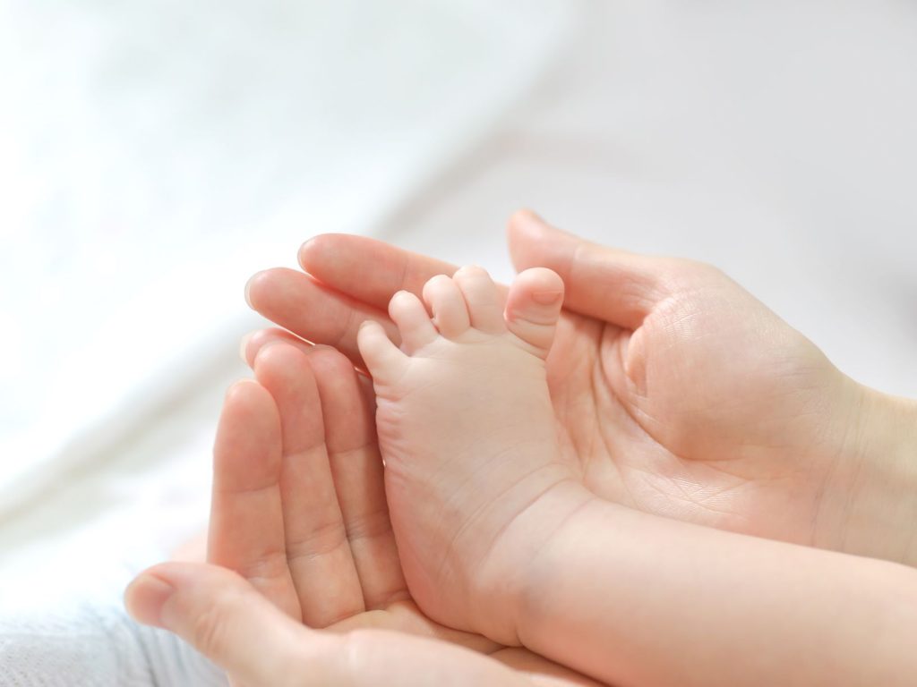 Foto em close das mãos de uma mulher segurando o pé de um bebê