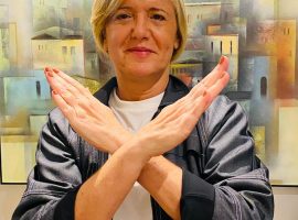 Foto da Margareth Goldenberg de braços cruzados na frente do corpo, com as mãos para cima, formando um X, gesto da campanha #QuebrandoBarreiras.