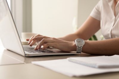Foto em close das mãos de uma líder mulher digitando no teclado de um laptop