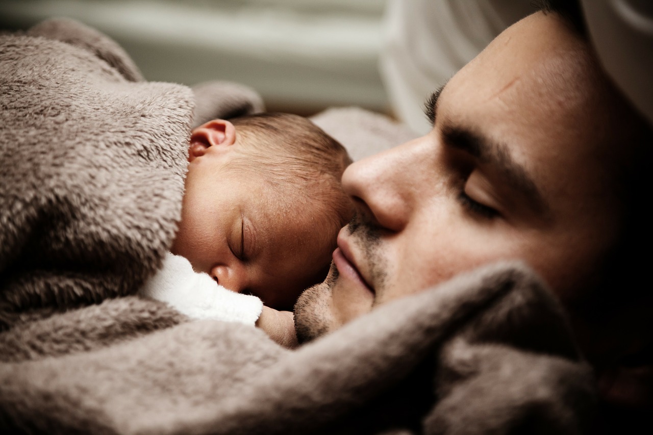 Foto em close de um bebê recém nascido deitado no colo de um homem.