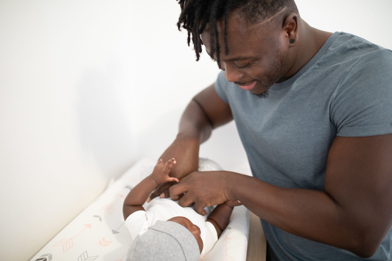 Foto de um homem trocando a fralda de um bebê.