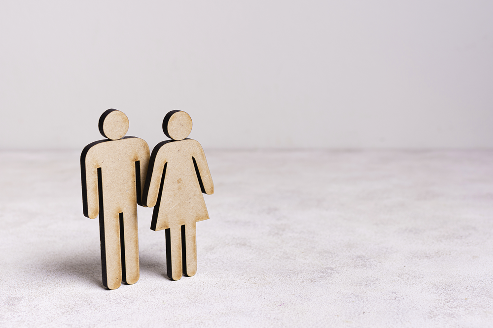 Foto de dois bonecos de madeira, um homem e uma mulher, em pé, em uma superfície plana.