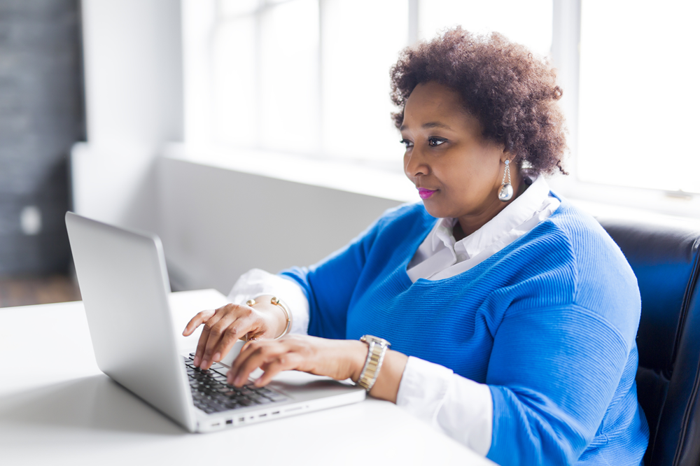 Foto de uma mulher negra gorda digitando no teclado de um laptop.