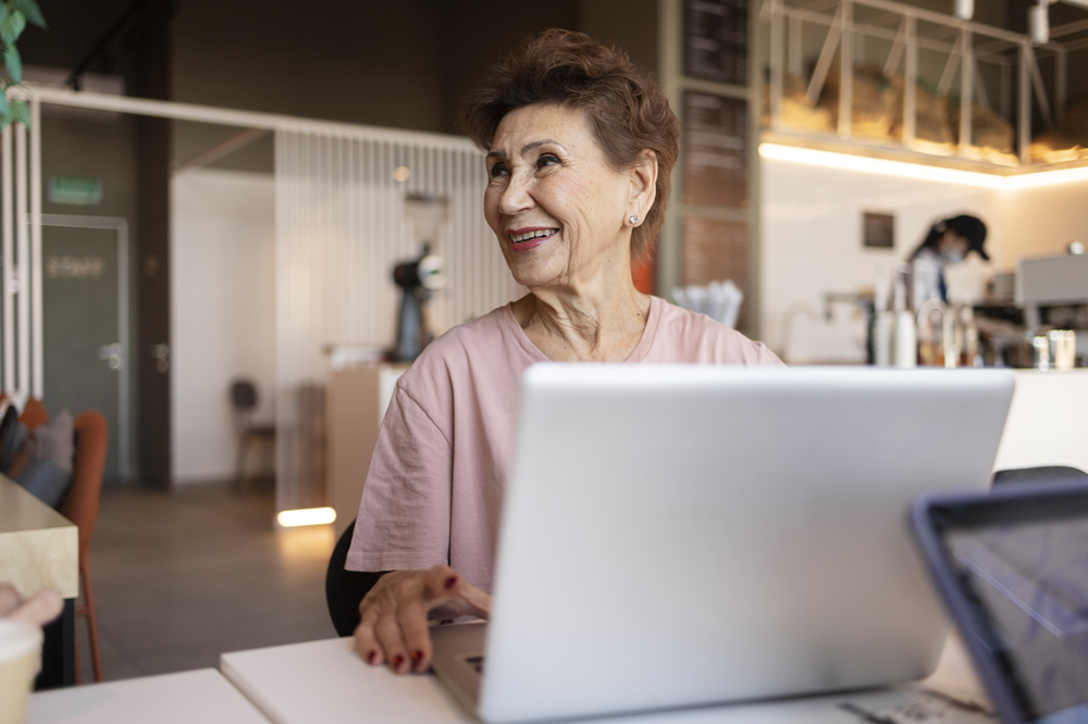 Foto de uma mulher com mais de 50 anos trabalhando com um laptop em uma cafeteria.