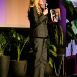 Foto de Margareth Goldenberg falando ao microfone durante sua participação no evento dos dez anos do MM360.