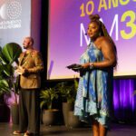 Foto de JP Polo e Letícia Vidica em cima do palco durante a apresentação do evento do Movimento Mulher 360.