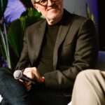 Foto de Marco Castro, sentado em uma poltrona branca, no palco durante sua participação do painel com CEOs.