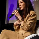 Foto de Ana Paula Padrão, mulher branca com cabelos lisos na altura dos ombros. Fala ao microfone enquanto participa do painel Cultura e Mídia.