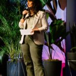 Foto de Karina Chaves falando ao microfone durante sua participação no evento dos dez anos do MM360.