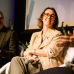 Foto de Juliana Sztrajtman, sentada em uma poltrona branca, no palco durante sua participação do painel com CEOs.